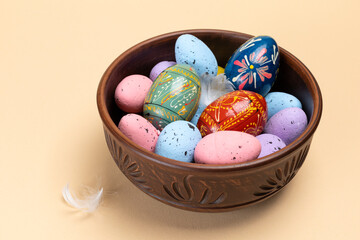 Bowl with colored Easter eggs on the beige background.