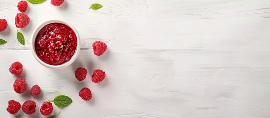 A white bowl filled with vibrant red raspberries, topped with fresh green leaves, set against a...