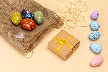Easter eggs on a sackcloth bag and a gift box on the beige background.