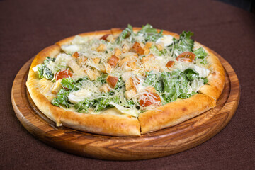 pizza with lettuce, tomatoes, cheese, croutons and egg on a wooden board. Brown background.