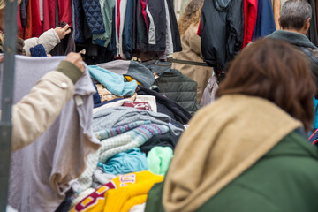 Obraz premium People choosing second-hand clothes at a flea market. Sustainable lifestyle, thrifting and upcycling concept.