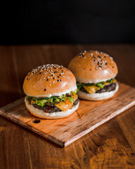 Side of two hamburger with sesame seeds on a toasted bun, sitting on french fries on wooden plate