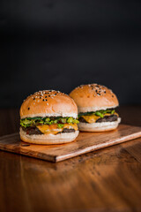 Portrait of two hamburger with sesame seeds on a toasted bun, sitting on french fries on wooden plate