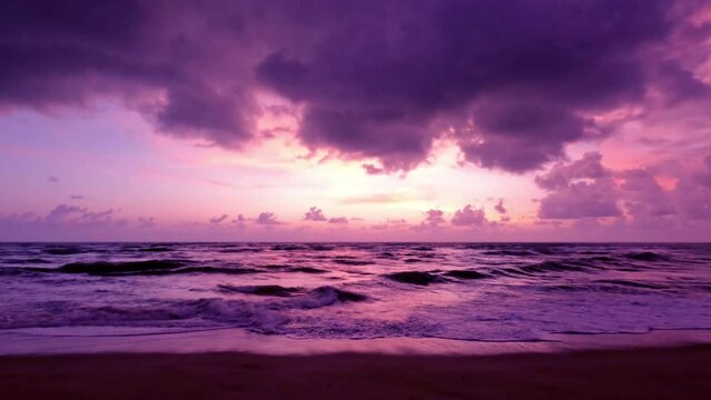 4k Slow motion sunset beach n purple blue colorful sky or violet storm cloud over sea water n calm ocean wave in tropical summer sunlight n sun ray at evening twilight coast or seashore, aerial view 