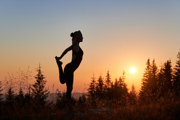 Young female meditating opposite to sunrise. Early morning workout on fresh air. Silhouette of girl practicing yoga in mountains in the morning.