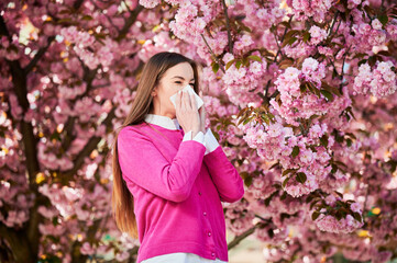 Woman allergic suffering from seasonal allergy at spring in blossoming garden at springtime. Woman...