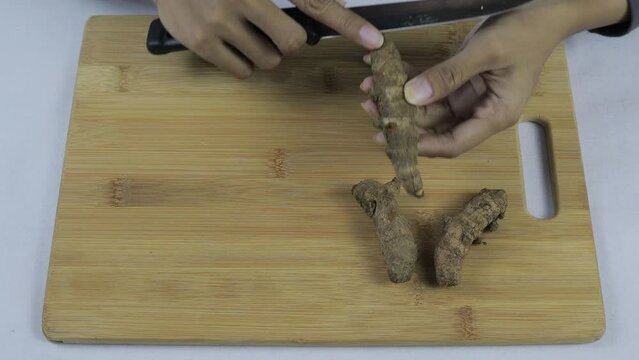 Close up view of Asian woman peeling turmeric (Curcuma longa) on wooden cutting board