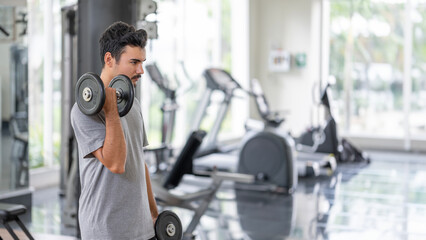 Focused young man performing a bicep curl in a modern gym, showcasing strength and determination....