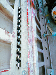 A spiral drill bit is on a wall. The wall is red and has a lot of holes