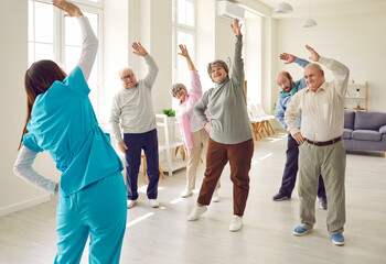 Nurse or physiotherapist doing healthy stretching exercises for wellness and health with a group of seniors. Elderly people working out in fitness class of nursing home with female instructor.