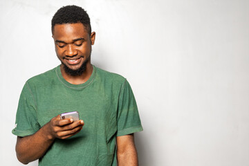 photo of young African american guy using smartphone. African man wearing green shirt, Texting,...