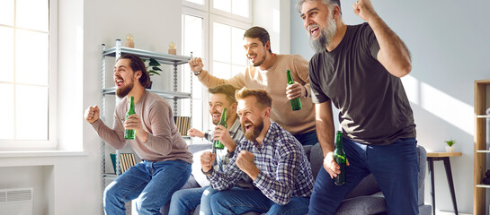 Male football fans watching soccer on tv at home. Group of emotional friends sitting on sofa with beer bottles and celebrating victory of their favorite team. Friendship, entertainment - obrazy, fototapety, plakaty