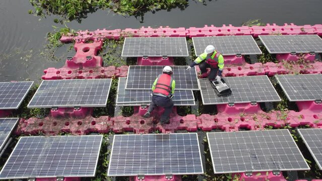 Aerial top view two technician workers use laptop and tools to check and maintenance solar cell panels over water reservoir.