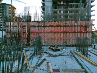 A construction site with a large building in the background. The building is being constructed with scaffolding and is surrounded by a lot of metal poles