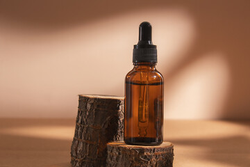Amber glass dropper bottle on a tree stump. Natural cosmetics, serum with floral extracts for skin care.