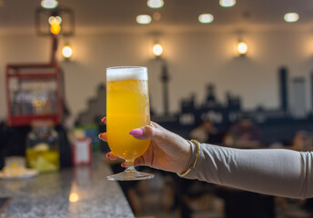 Woman's hand holding glass of beer up high in restaurant or pub