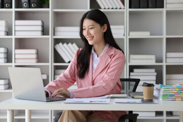 Young beautiful asian businesswoman working with laptop and paperwork on desk in office.