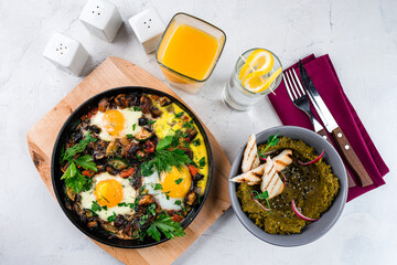 Breakfast fried eggs with bacon, onion, mushrooms, zucchini, herbs and green snack with bread and glass of juice.