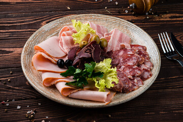Meat plate with slices of sausage, ham, bacon, olives and greens.