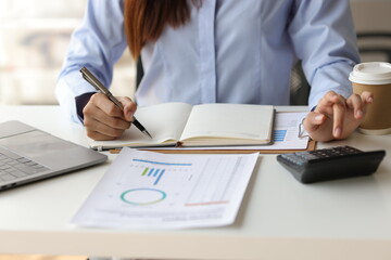 Businesswoman working on financial documents on the desk in the office is writing notes and calculating income and expenses.