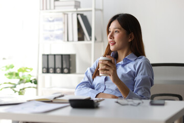 Portrait of a charming Asian businesswoman in casual clothes drinking hot coffee and relaxing during a break in the office.