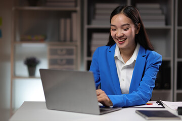 Attractive Asian businesswoman working overtime with documents on desk in office.