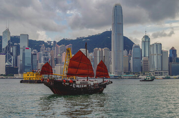 Traditional Chinese junk with red sails and Hong Kong Hongkong skyline in Victoria Harbor with...