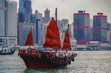 Traditional Chinese junk with red sails and Hong Kong Hongkong skyline in Victoria Harbor with...
