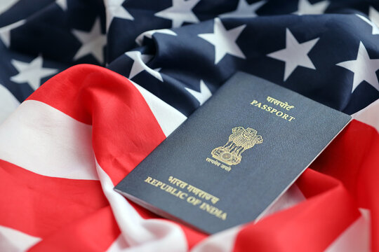 Blue Indian passport on United States national flag background close up. Tourism and diplomacy concept