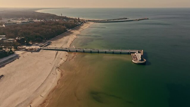 Drone footage captures Kołobrzeg pier, sandy beach with tourists.