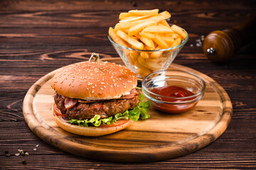 American food beef burger with bacon, tomato and lettuce with french fries and ketchup.