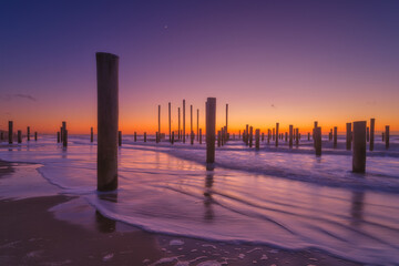 A seascape during sunset. Pillars on the seashore. Bright sky during sunset. Reflections on the seashore. A sandy beach at low tide. Travel image. - 749250992