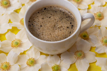 Morning white cup of coffee with foam and white anemone flowers on the table