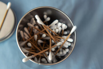 Top down view heap of cotton buds in stainless steel container with blue bed sheet as background
