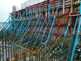 A construction site with a large building in the background. The building is being constructed with scaffolding and is surrounded by a lot of metal poles