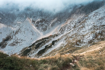 Hiking trail high in the mountains with lots of rocks and dry grass in the autumn with clouds covering peaks, Durmitor, Montenegro