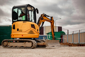 A mini excavator rams the ground with a vibrating plate. Laying of underground sewer pipes and communications during construction. soil compaction. Earthworks, excavation. © Anoo