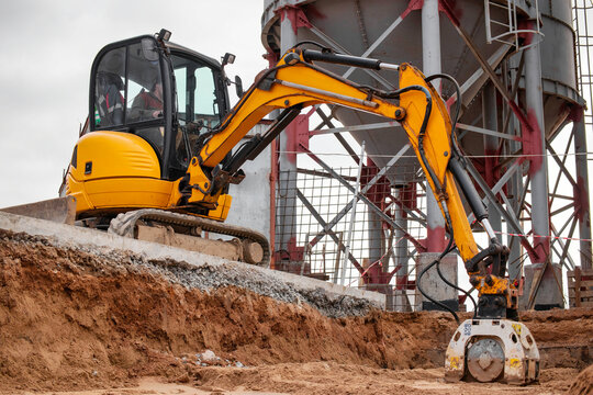 A mini excavator rams the ground with a vibrating plate. Laying of underground sewer pipes and communications during construction. soil compaction. Earthworks, excavation.