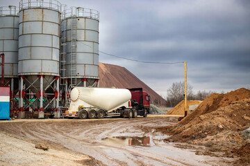 Large truck for transporting cement. A cement truck unloads cement at a concrete plant. Concrete...