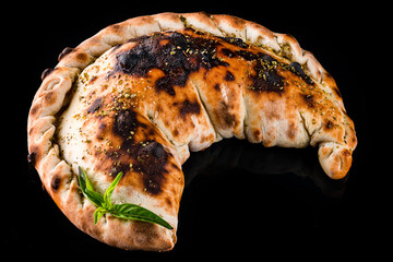 Dinner Neapolitan closed pizza calzone with basil and spices isolated on black.