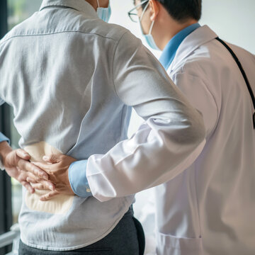 Doctor is diagnosing a patient's back pain in a hospital examination room. A male with back pain sees a doctor for treatment

