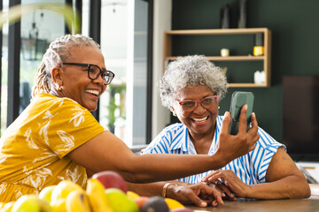 Senior African American woman and biracial woman share a joyful moment over a smartphone at home