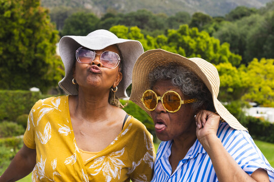 Senior African American woman and biracial woman make playful faces, wearing sun hats, on vacation