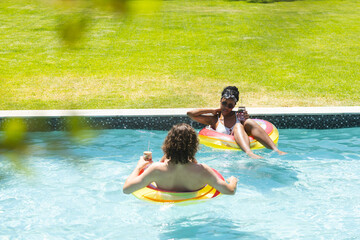 Diverse couple young African American woman and Caucasian man relax on floaties in a pool