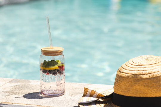 A fruit-infused water jar sits beside a straw hat by a pool