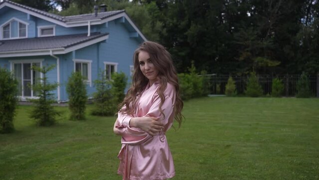 A woman in a pink robe standing in front of a blue house