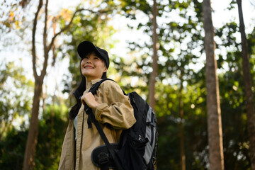 Relaxed young woman with backpack trekking in forest and enjoying nature