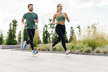 Active couple jogging together in an urban park, with tall grass and modern design.