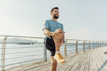 Man in athletic gear doing knee stretches on a sunny boardwalk by the sea.