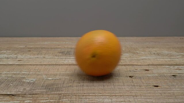 An orange rolls on a wooden surface on a gray background.